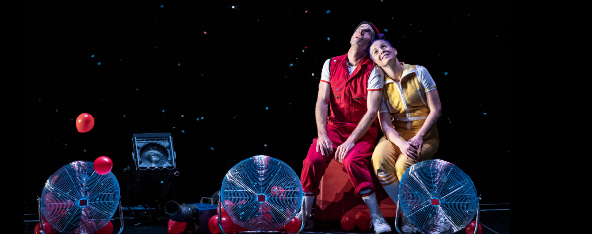 two performers seated in front of rotary fans